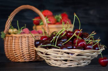 Olgun kirazlarla dolu bir tabak ve arka planda bir sepet dolusu böğürtlen..