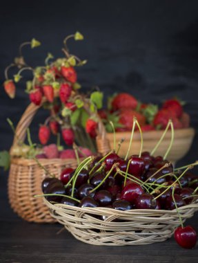 Olgun kirazlarla dolu bir tabak ve arka planda bir sepet dolusu böğürtlen..