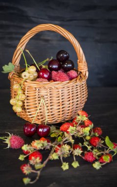 Bir sepet dolusu olgun böğürtlen ve siyah ahşap yüzey üzerinde çilek..