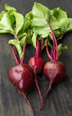 Tahta arka planda yaprakları olan üç taze kırmızı pancar..