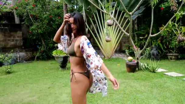 Hermosa mujer asiática joven con bikini y kimono de playa de verano o pareo sarong en el jardín tropical. Vacaciones de verano — Vídeo de stock