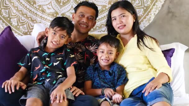 Familia del sudeste asiático pasar tiempo en casa. Padres y niños indonesios o malasiáticos felices acostados en la cama divirtiéndose juntos — Vídeo de stock