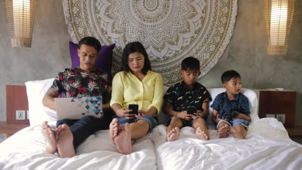 Ινδονησιακή ή μαλασιατική οικογένεια εθισμένη στην ψηφιακή τεχνολογία. Οικογένεια στο σπίτι χρησιμοποιώντας smartphones. Μαμά, μπαμπάς και παιδιά παθιασμένα με συσκευές που χρησιμοποιούν υπερβολικά τα μέσα κοινωνικής δικτύωσης, παίζουν παιχνίδια ή βλέπουν βίντεο — Αρχείο Βίντεο