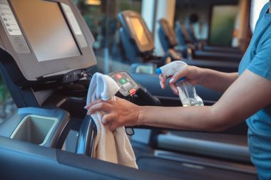 Spor salonu temizliği ve dezenfeksiyon. Enfeksiyon önleme ve salgının kontrolü. Spor salonunda koşu bandını temizlemek için mendil ve alkol dezenfektanı kullanan personel. Anti-Covid-19 önlemleri
