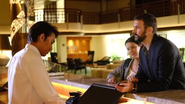 Συνεργάτες ή συνάδελφοι κάνουν check-in στο ξενοδοχείο. Νεαρό ζευγάρι και ρεσεψιονίστ στο ταμείο του ξενοδοχείου — Αρχείο Βίντεο