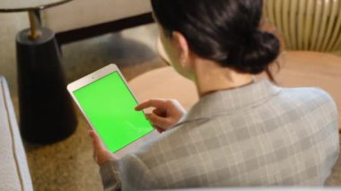 Genç iş kadını yeşil ekranlı tablet kullanıyor. Tablet tutan kadın, sayfaları kaydırıyor. Omzunun üstünden bak.