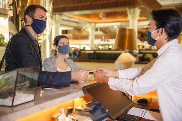 커플과 접수 담당자가 병원 카운터에서 의료용 마스크를 쓰고 바이러스 예방 조치를 취하고 있습니다. 사업 차 출장중인 커플이 호텔에서 체크인하는 모습 로열티 프리 스톡 사진