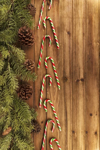 Candy canes and Christmas tree branches on natural wooden table in background. Directly above.