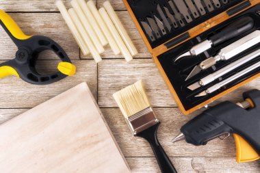DIY araç hemen üstüne beyaz bir ahşap tahta üzerinde kümesi. Tutkal tabancası, boya fırçası, kelepçe ve hassas bıçak.