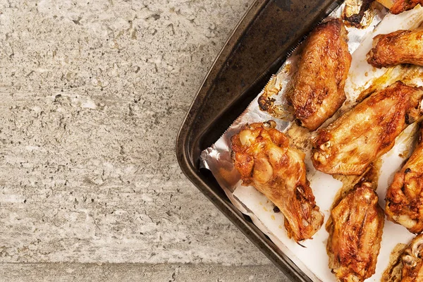 Barbecue chicken wings on an old cooking pan, concrete texture in background. Directly above.