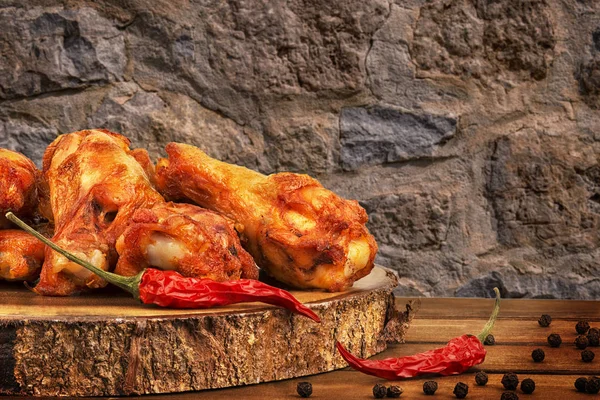 赤唐辛子と木製のテーブルの胡椒手羽先 バック グラウンドで石の壁 — ストック写真