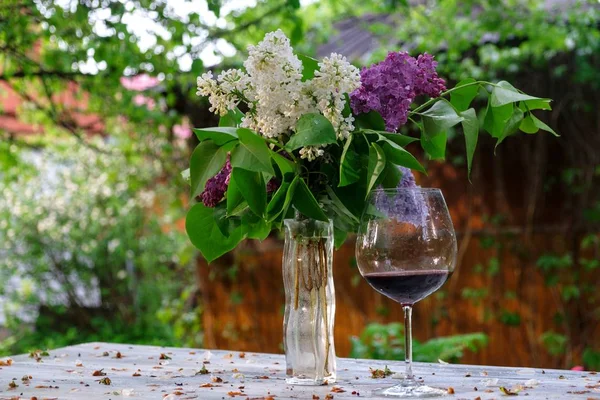 Fliederstrauß in einer Glasvase und ein Glas Rotwein Stockfoto