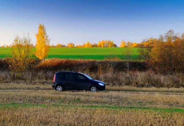 Αυτοκίνητο ταξιδεύει στο δρόμο με χωράφια και τα φθινοπωρινά δέντρα στο ζεστό ηλιοβασίλεμα φως Royalty Free Φωτογραφίες Αρχείου
