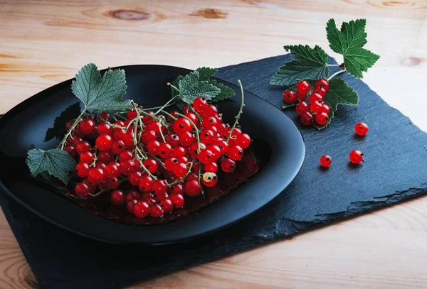 Redcurrants on a black plate on a wooden table — Stock Photo, Image