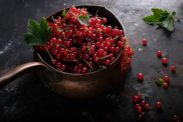 Red currants and leaves in old copper bowl on dark background — Stock Photo, Image