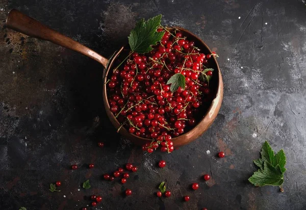 Röda vinbär och löv i gammal koppar skål på mörk bakgrund — Stockfoto