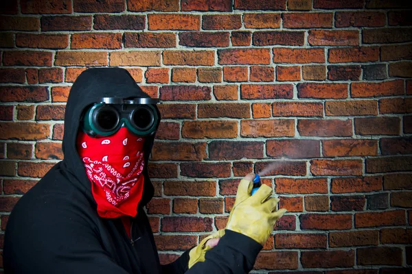 Hidden man with hood and scarf with spray in front of a brick wa