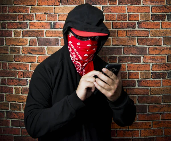 Κρυφός άνθρωπος με κουκούλα και κασκόλ χρησιμοποιώντας το κινητό τηλέφωνο μπροστά από ένα — Φωτογραφία Αρχείου