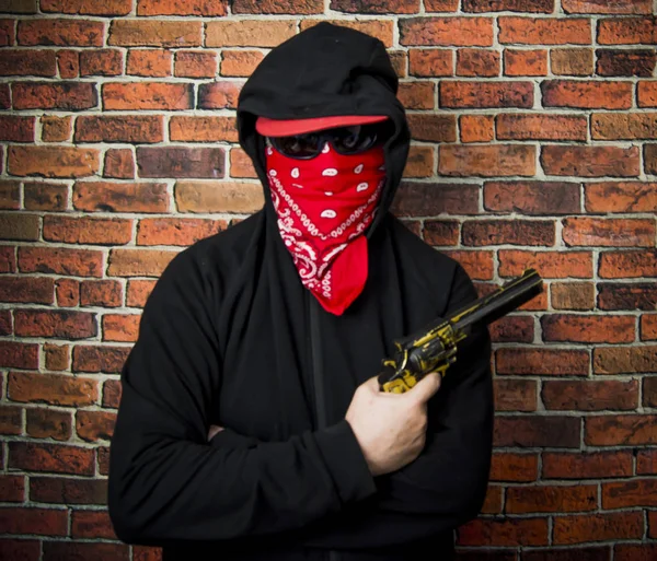 Verborgen man met capuchon, sjaal en pistool voor een bakstenen muur — Stockfoto