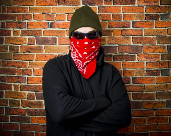 Hidden man with hood and scarf in front of a brick wall
