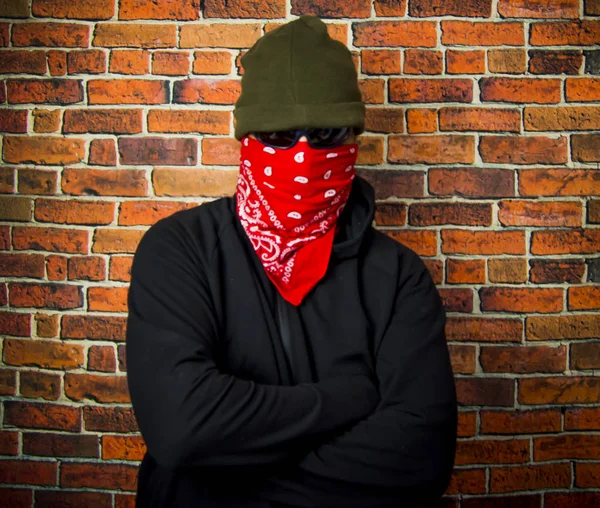 Прихований чоловік з капюшоном і шарфом перед цегляною стіною — стокове фото