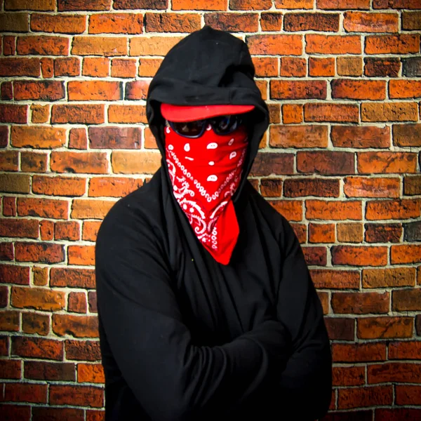Hidden man with hood and scarf in front of a brick wall