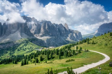 Gardena Geçidi 'ndeki yeşil çayırlar boyunca uzanan dağ yolu. Arka planda dramatik Dolomitler var. Güney Tyrol, İtalya. Alp yürüyüş yolu ve manzarası