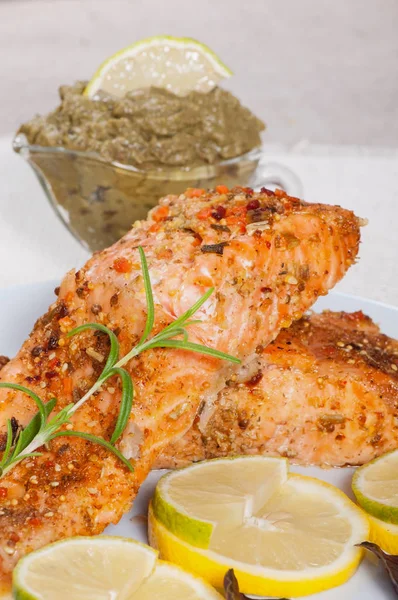 Grilled salmon with spices, lemon and basil, on a light plate.