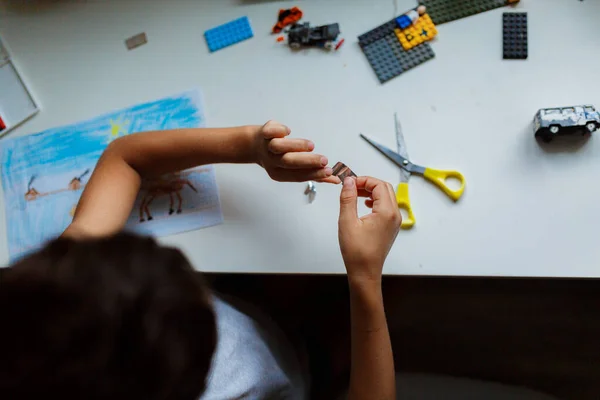 Gri tişörtlü, elinde makasla oturan Asyalı siyah saçlı çocuk farklı şekillerde kesilmiş.