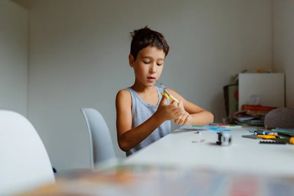 dark-haired boy draws a picture with pencils while sitting at a white table