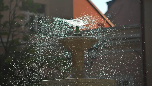 Droplets dispersing from a fountain and buildings in background — Stock Photo, Image