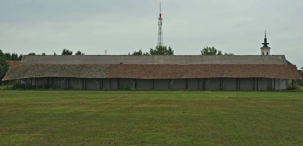 Largo cobertizo junto al establo en un gran campo con iglesia y torre de radio en el fondo —  Fotos de Stock