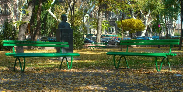 Парк с двумя зелеными скамейками, опавшими листьями и памятником осени — стоковое фото
