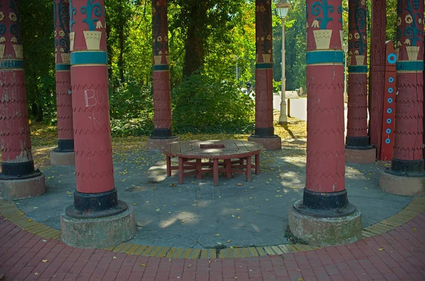 Banco redondo de madeira vermelho em um parque cercado por grandes pilares vermelhos — Fotografia de Stock