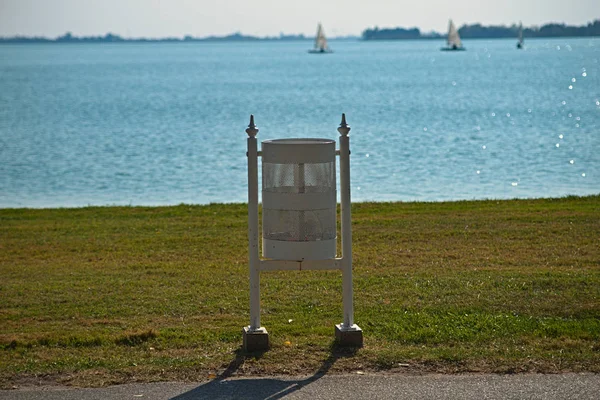 Poubelle blanche sur la promenade regardant le champ d'herbe et le lac — Photo