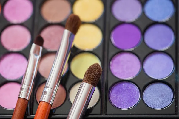 Makeup brushes on background with colorful powder. Selective focus, macro shooting.