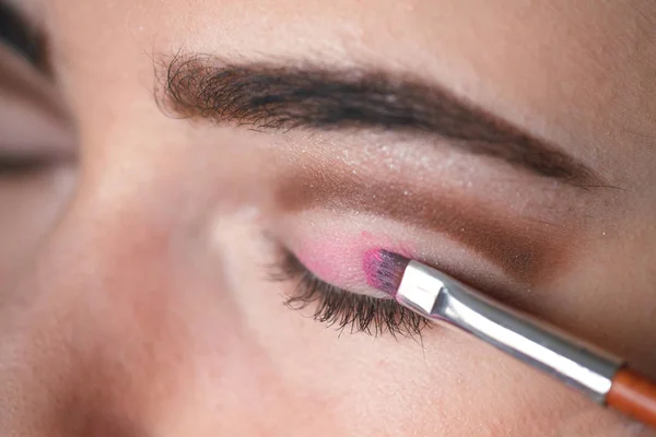 Sombra de ojos aplicando, maquillaje para los ojos de cerca. Mujer joven aplica sombra de ojos de color rosa con maquillaje cepillo . — Foto de Stock