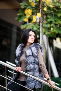 Şık kadın kürk yelek şehirde yürüyüş. Kentsel sokak stil, moda trendi. Seksi güzel kadın moda açık fotoğrafı