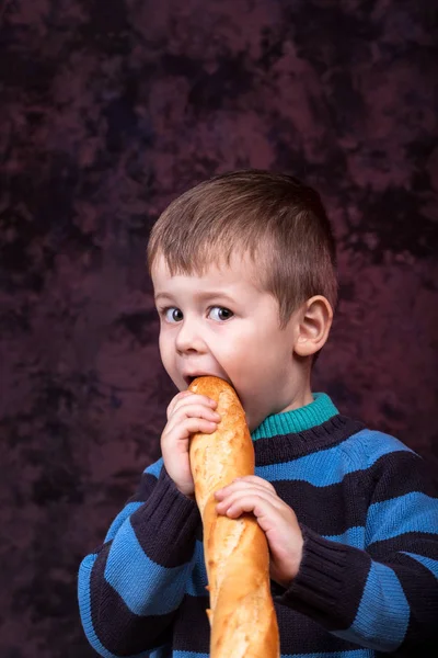 Милый Ребенок Держит Кусает Французский Хлеб Темно Красном Фоне Мальчик — стоковое фото