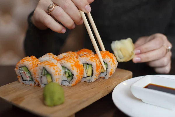 Young woman in wig eating sushi by chopsticks