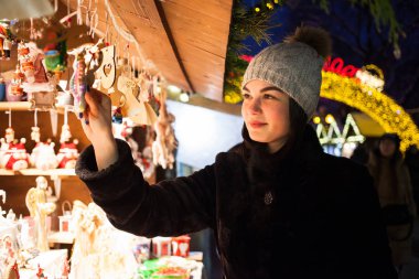 Mutlu genç kadın Noel dekorasyon Market seçme. Bere şapka örgü model giyen şık kürk manto. Açık fotoğraf
