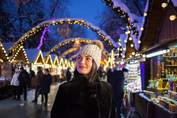 Sokakta poz güzel mutlu gülümseyen kız. Neşeli Noel arka plan üzerinde adil. Bere şapka örgü model giyen şık kürk manto. Açık fotoğraf