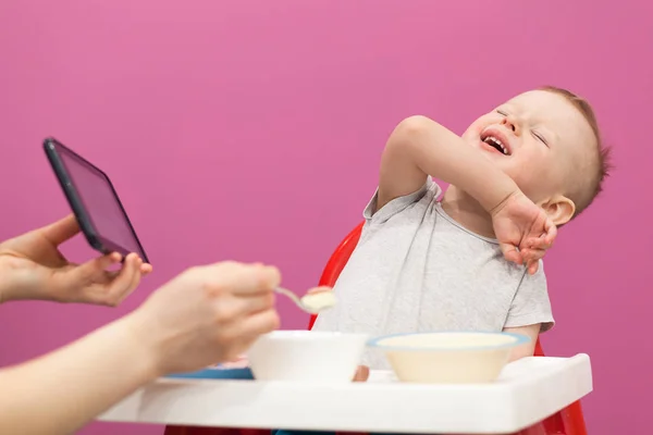 Küçük çocuk patates püresi yemek istemiyor. Tablet üzerinde karikatür izlerken çocuk evde kahvaltı yiyor