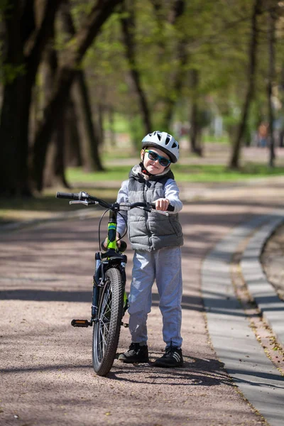 Little boy learns to ride a bike in the park. Cute boy in sunglasses rides a bike. Happy smiling child in helmet riding a cycling.