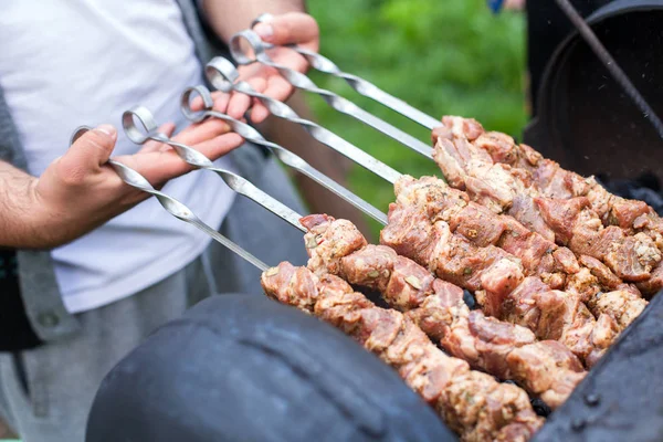 Руки шеф-повара жарят барбекю дома на открытом огне, искажая металлические палочки сочными ломтиками мяса. Летний пикник на природе — стоковое фото