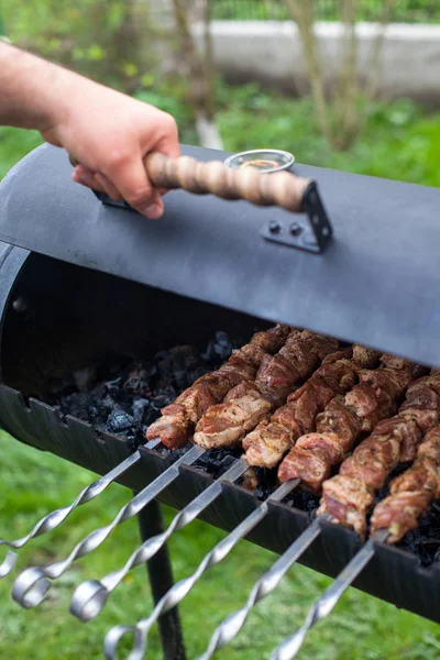 Bir adamın eli metal bir brazier açar. Barbekü taze domuz eti doğrayın dilimleri. Geleneksel doğu yemeği şiş kebap. — Stok fotoğraf