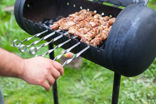 チーフクッカーの手は、肉のジューシーなスライスで金属の棒を傾け、暖炉の上で自宅でバーベキューを焼いています。自然の中で夏のピクニック — ストック写真