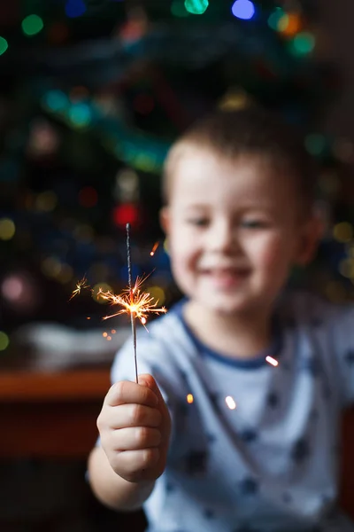 Schönes kleines Kind mit brennender Wunderkerze am Silvesterabend, Bengalfeuer. Der Schwerpunkt liegt auf Feuerwerk. glücklicher Junge mit Wunderkerzen auf verschwommenem Weihnachtshintergrund. — Stockfoto