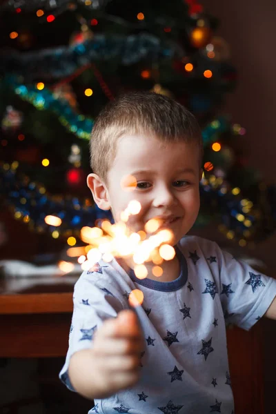 Schönes kleines Kind mit brennender Wunderkerze am Silvesterabend, Bengalfeuer. es gibt einen Hintergrund mit bunten Lichtern. — Stockfoto