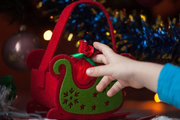 Die Kinderhand greift nach einem Neujahrsgeschenk unter dem grünen Baum. Frohes neues Jahr und Weihnachten. — Stockfoto